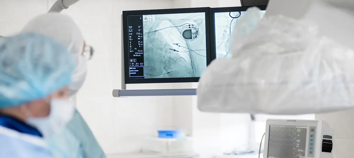 Medical team in surgical attire performing a procedure in a hospital operating room, with monitors displaying real-time imaging and vital signs.