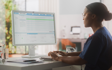 Female medical health care professional working on a desktop computer in a hospital office.