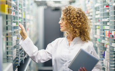 Female scientist or technician with curly hair holding a tablet and examining equipment or samples in a laboratory or data storage facility.