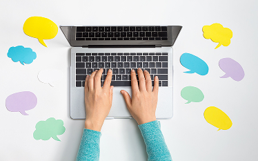 Top-down view of hands typing on a laptop keyboard, with cloud-shaped icons scattered on the white desk surface.