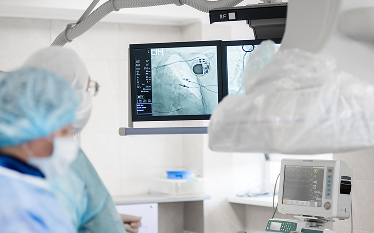 Medical team in surgical attire performing a procedure in a hospital operating room, with monitors displaying real-time imaging and vital signs.