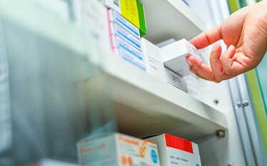 Hand reaching for a box of medication from a shelf in a pharmacy or medical storage unit.