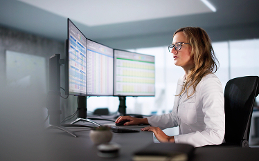 Person working at multiple computer monitors displaying data tables, illustrating monitoring targets for clinical trials in the EU