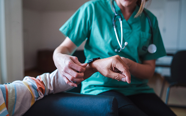 Nurse adjusting a wearable device on a patient’s wrist to capture patient experience data