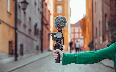 Hand holding a camera with a microphone, representing content creation