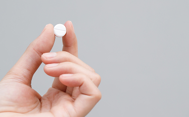 Hand holding a white tablet between fingers, representing discussion of adverse drug reaction monitoring and signal detection