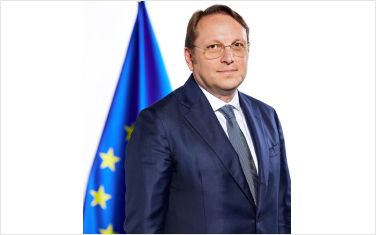 Portrait of Commissioner for Health and Animal Welfare Olivér Várhelyi standing in front of a European Union flag