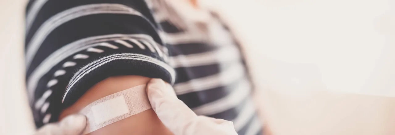 Gloved hands applying a plaster on the arm of a patient after vaccination