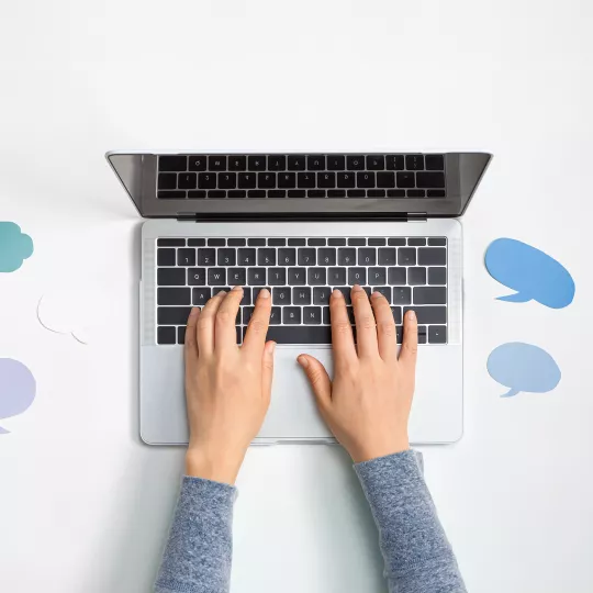 Human hands typing on the keyboard of a laptop placed on a table in the middle of stickers shaped to evoke dialogue
