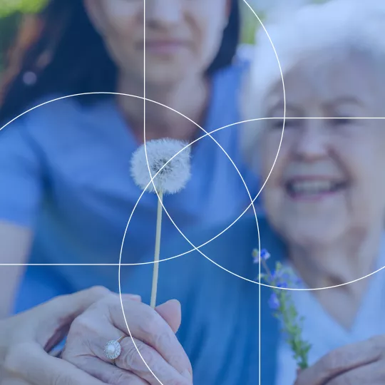Nurse seen helping an elderly person pick up and hold a dandelion