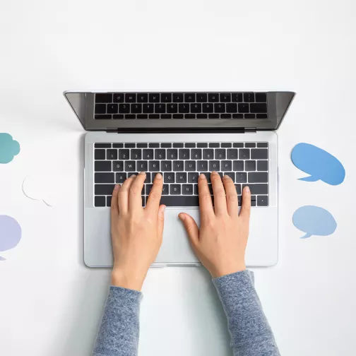 Human hands typing on the keyboard of a laptop placed on a table in the middle of stickers shaped to evoke dialogue