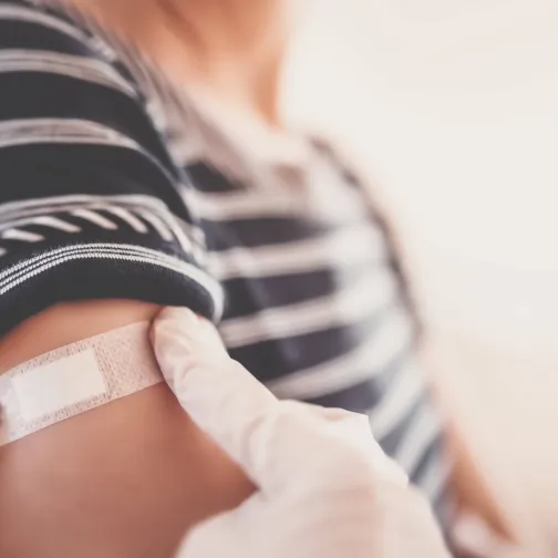 Gloved hands applying a plaster on the arm of a patient after vaccination
