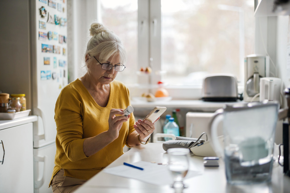 Woman reading the label on a pill jar with her mobile in her other hand